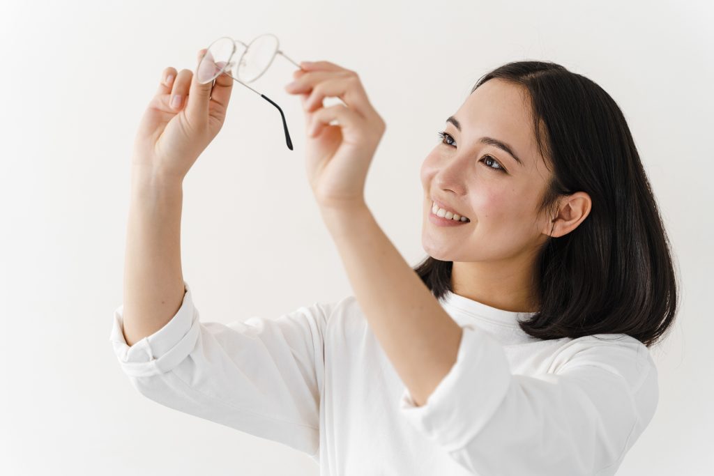 Beautiful woman checking the cleanliness of glasses. Girl posing on a white wall background.